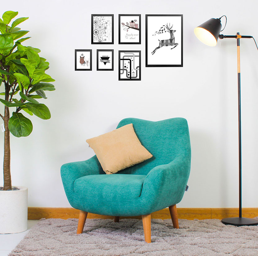 Ghế sofa vải đơn màu xanh ngọc với gối tựa màu be, đèn sàn đen, và bộ sưu tập tranh đen trắng treo trên tường trắng
