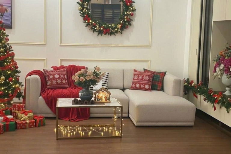 Phòng khách ấm cúng với sofa chữ L, bàn trà và không gian trang trí Giáng Sinh sang trọng gồm cây thông, vòng nguyệt quế và phụ kiện Noel
